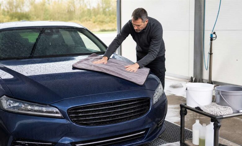 Fahrzeugpfleger trocknet den nassen Autolack auf einem professionellen Waschplatz